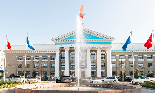 Building of Bishkek city council  with fountain in front on sunny day.