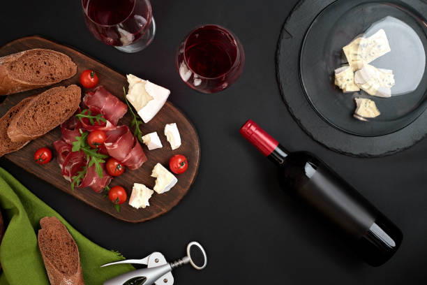 istock Red wine, cheese, cherry tomato, bread and prosciutto on wooden board over black backdrop, top view, copy space 951306872