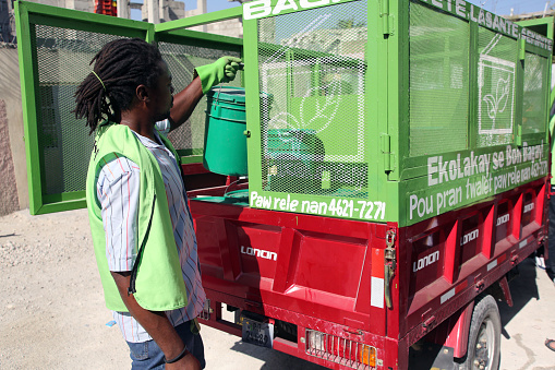 Port-au-Prince, Haiti - March 14, 2018: A SOIL employee loads  full buckets from EkoLakay Ecosan home composting toilet clients into a motorized tricycle cart that will take them to a composting center. SOIL provides and services the toilets, which provide the basic elements, human waste and shredded vegetable matter, of compost, for about $4 a month.