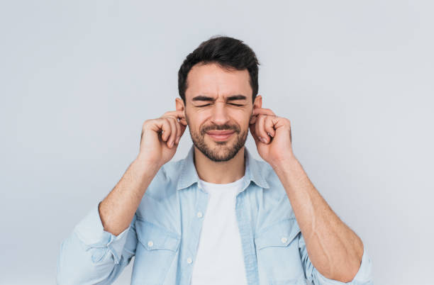 retrato de estudio horizontal de guapo barbudo joven masculinos tapones oídos con descontentaron expresión como oye ruido molesto, aislado sobre pared blanca. concepto personas y emoción - men shouting human hand sound fotografías e imágenes de stock