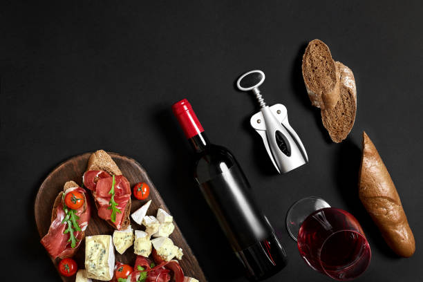 istock Red wine, cheese, cherry tomato, bread and prosciutto on wooden board over black backdrop, top view, copy space 951344112