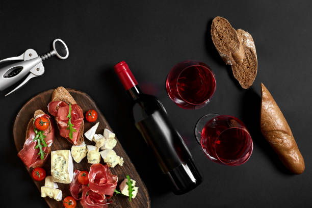 istock Red wine, cheese, cherry tomato, bread and prosciutto on wooden board over black backdrop, top view, copy space 951344408