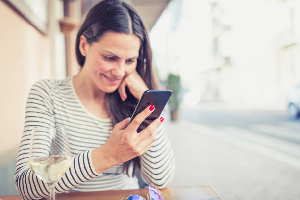 istock Young woman drinking white wine at restaurant, using mobile phone 951344720