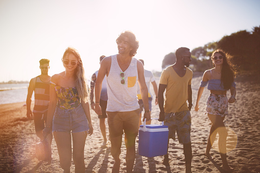 Multi-ethnic hipster friends carrying cooler box on the beach, ready for summer island beach party
