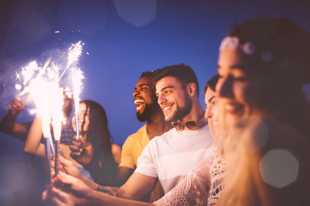 istock Young multi-ethnic hipster friends celebrating with fireworks at beach party 951356250