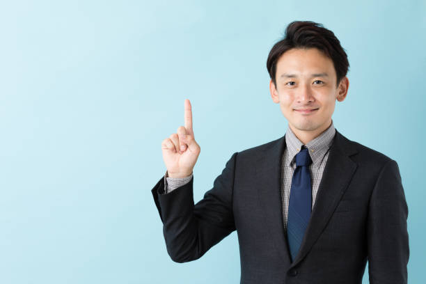 portret van aziatische zakenman geïsoleerd op blauwe achtergrond - wijsvinger stockfoto's en -beelden
