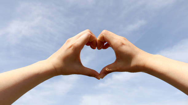istock A woman's hand forming a heart to the blue spring sky. 951364366