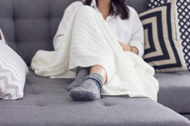 istock Young woman sitting on sofa covered in blanket, focus on her gray socks 951396680