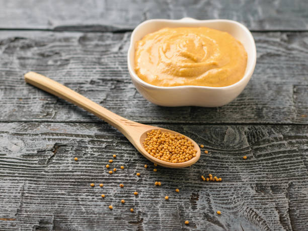 istock Spoon with mustard seeds and bowl with mustard sauce on dark rustic table. 951405600
