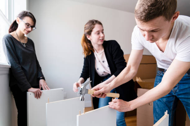 the family moving in to the new apartment. the young 30 years old man and two teenage girls, sisters, unboxing and assembling furniture. - independence lifestyles smiling years imagens e fotografias de stock