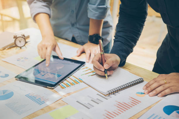 istock Startup Concept.Young businessman holding pen Writing a summary report on a notebook and A friend pointing on tablet to explain the work plan at home office. 951431688