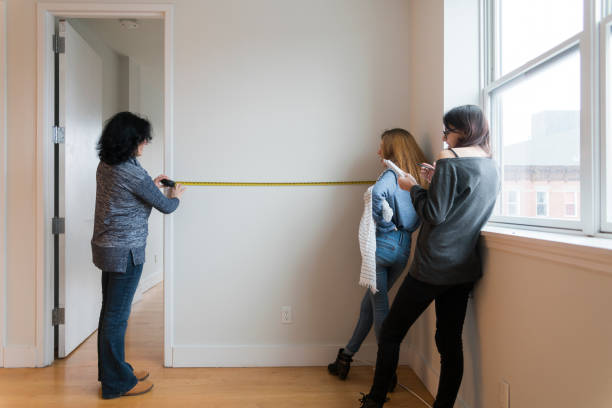 The young attractive woman, the mother, and her two teenage daughters measuring the new apartment for future furniture placement The young attractive woman, the mother, and her two teenage daughters measuring the new apartment for future furniture placement in the rental apartment in Brooklyn, New York, USA measuring a room stock pictures, royalty-free photos & images