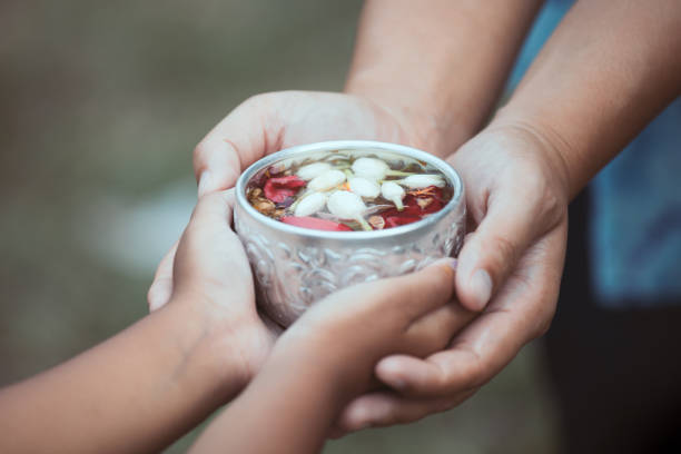 Asian little child girl and mother holding a little bowl that have flower leaf in water together for pouring on hands of elderly Asian little child girl and mother holding a little bowl that have flower leaf in water together for pouring on hands of elderly to respect grandparents for celebrate Songkran in new year holding child flower april stock pictures, royalty-free photos & images