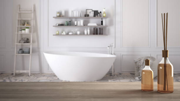 istock Wooden table top or shelf with aromatic sticks bottles over blurred classic bathroom with bathtub, white architecture interior design 951455140