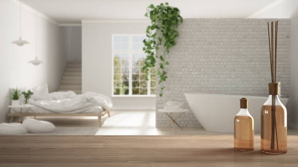 istock Wooden table top or shelf with aromatic sticks bottles over blurred minimalist bathroom and bedroom, white architecture interior design 951455220