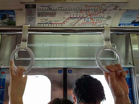 Close up of people's hands holding hanging support rings to keep them steady on the Tokyo Metro underground, whilst the train is moving.