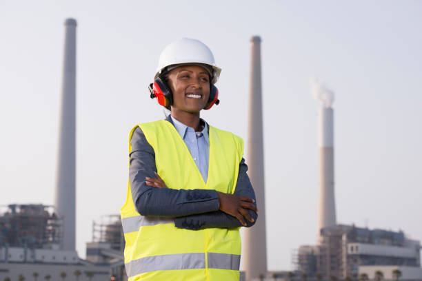 istock Engineer woman with crossed arms standing at a coal-fired power station, wearing reflective clothing, sound reduction headphones and work helmet, looking away. 951470430