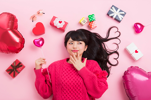 A young asian woman smiles surrounded by heart shaped balloon and gift boxes