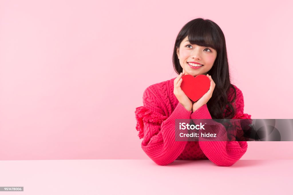 A woman in red sweater holding gift boxes An asian woman in red sweater smiles holding a heart shaped gift box in front of pink background Women Stock Photo