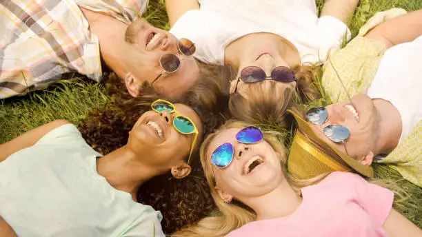 Multiethnic group of friends lying on grass, enjoying happy life and laughing