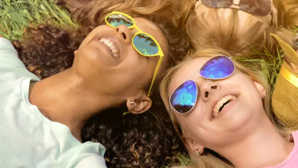 Close-up of friends faces, happy girls lying on grass, multiracial friendship