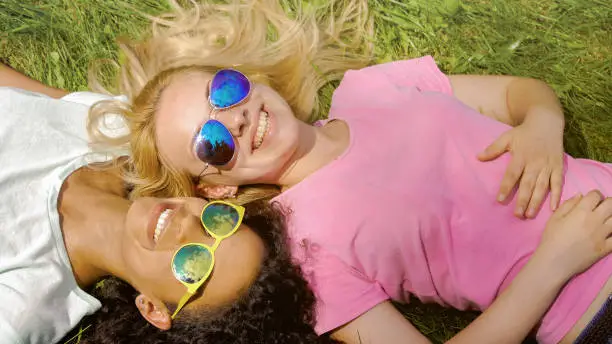 Two female friends lying on grass in park, enjoying summer weekend, friendship