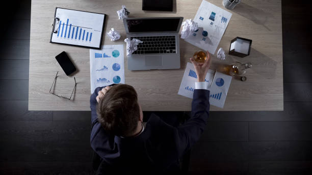 istock Upset businessman sitting at table and drinking alcohol, depression, top view 951480958