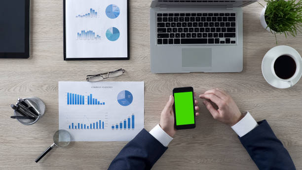 istock Businessman scrolling pages on green screen smartphone in office, top view 951481220