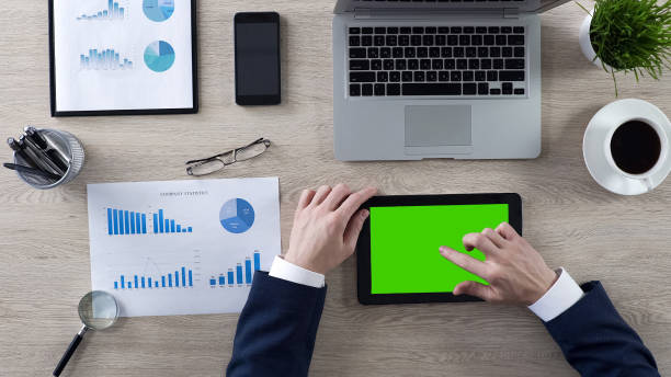 Businessman working on tablet with green screen, top view of workplace