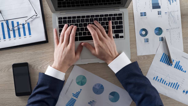 istock Man in classic suit analyzing company statistics and entering data on laptop 951483530