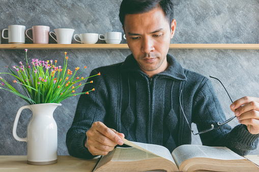 Asian man reading a book and holding glasses on table