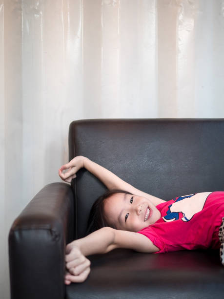 kleine asiatische kind mädchen kind dehnen sich auf dem sofa nach ihrer tagesschläfrigkeit - liegefahrrad stock-fotos und bilder