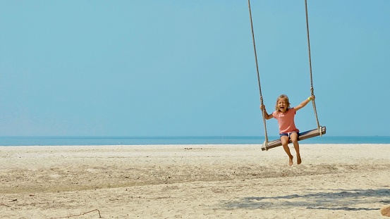 Teenage girl having fun swinging at the beach playground. Summer day evening \nCanon R5