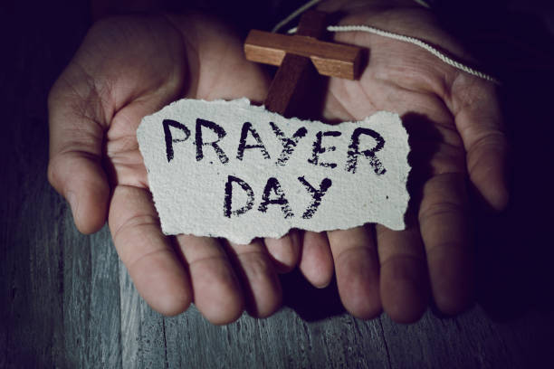 man with a crucifix and the text prayer day closeup of the hands of a young caucasian man with a wooden crucifix and a piece of paper with the text prayer day in them national day of prayer stock pictures, royalty-free photos & images