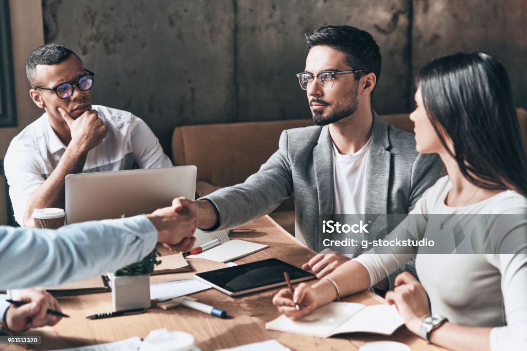 Mutual understanding. Young modern men in smart casual wear shaking hands while working in the creative office Business Stock Photo