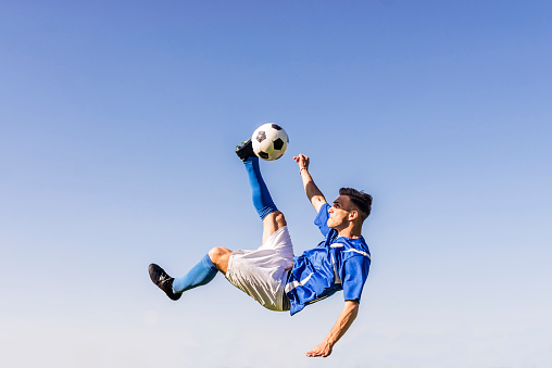 Determined bicycle kick on a soccer match! Photo of Football player doing overhead kick during bright sunny sumer day.
