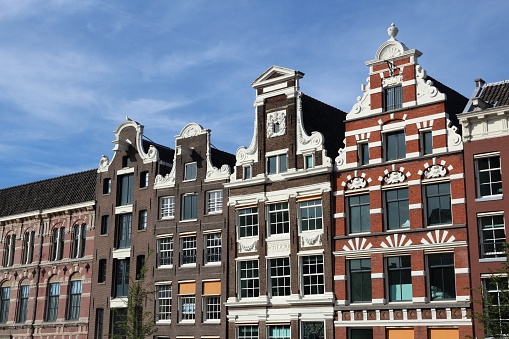 Amsterdam canal house facades at the Damrak with a blue sky in the background during summer.