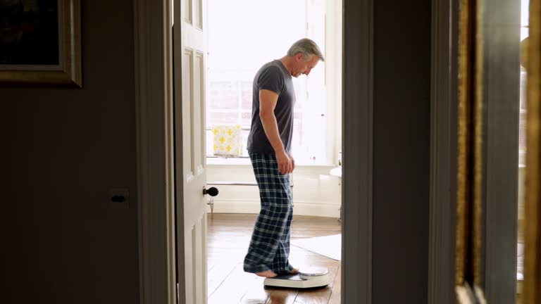 Senior man in pajamas stepping on bathroom scale