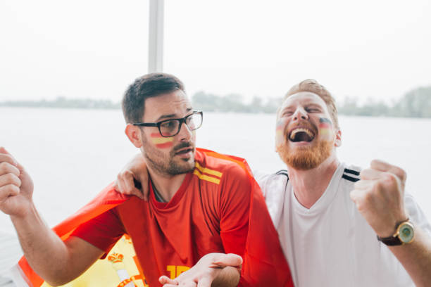 istock Friends watching soccer, supporting different teams hugging and watching a game toggether 951539614
