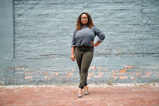 Portrait of an attractive and confident young woman standing against a gray wall outside