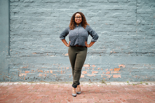 Portrait of an attractive and confident young woman standing against a gray wall outside