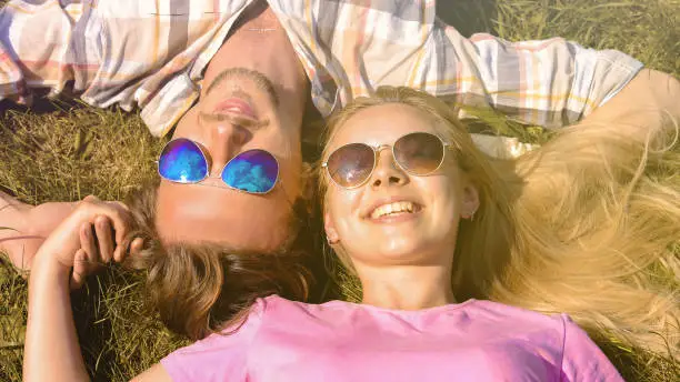 Young man and woman lying on grass, smiling, holding hands, enjoying holidays
