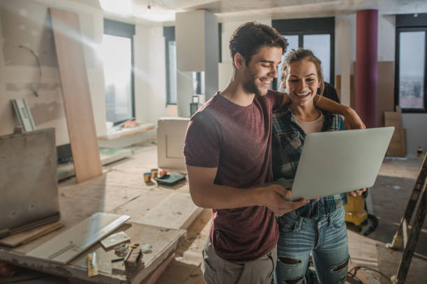 feliz pareja abrazado usando laptop estando en el sitio de construcción en su apartamento. - computer construction using laptop construction site fotografías e imágenes de stock