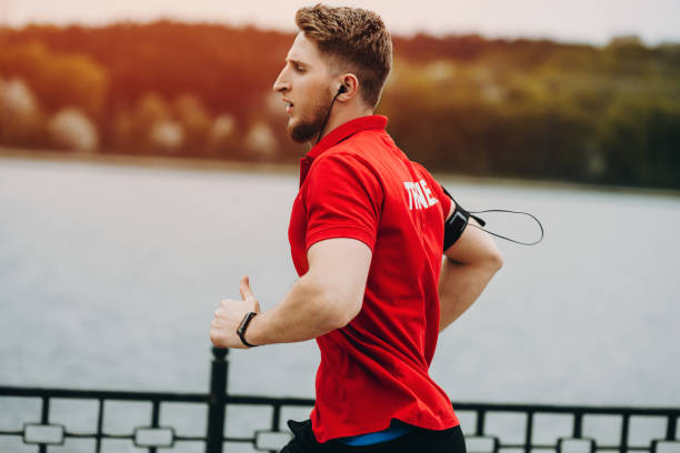 istock Attractive muscular man is running in a beautiful park with gadgets on hands. 951597968