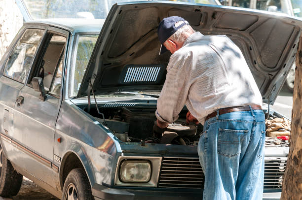 старик ремонтирует свой сломанный автомобиль yugo на улице. вид со спины. - old men car oil стоковые фото и изображения