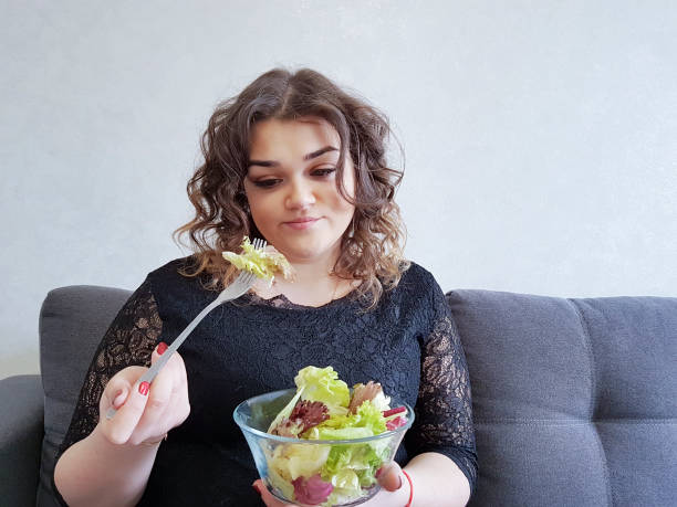 plein de belle fille sur le canapé avec un régime salade - overweight women salad frustration photos et images de collection