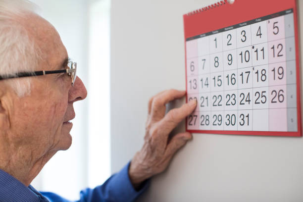 confundida senior hombre con demencia observando a calendario de pared - one person lifestyles 80 plus years indoors fotografías e imágenes de stock