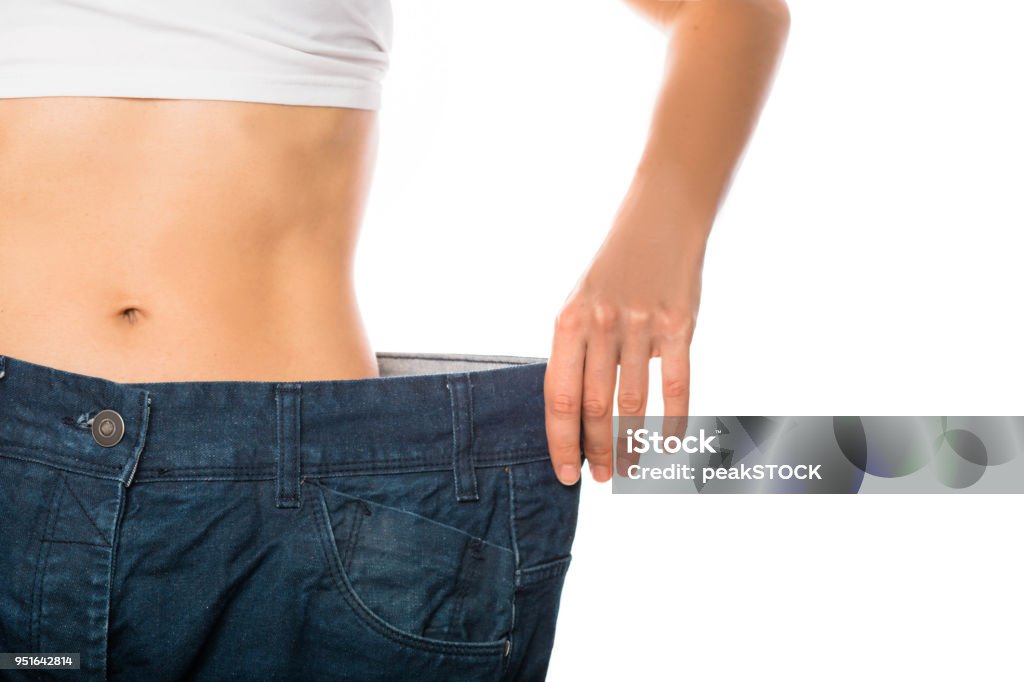 Weight loss and slimming Slim stomach of young woman, thin body with perfect waist, showing her jeans after successful diet or sport training on isolated background. Weight loss and slimming Dieting Stock Photo