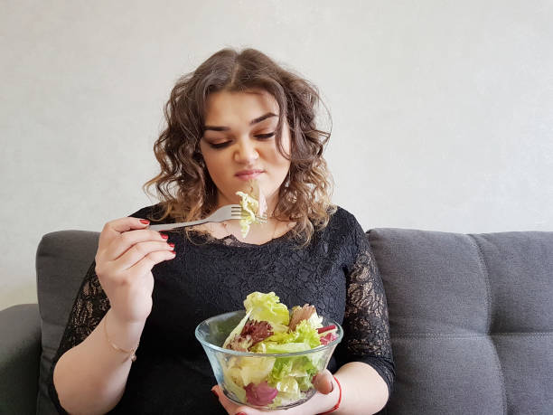 muito linda garota no sofá com uma dieta de salada - overweight women salad frustration - fotografias e filmes do acervo