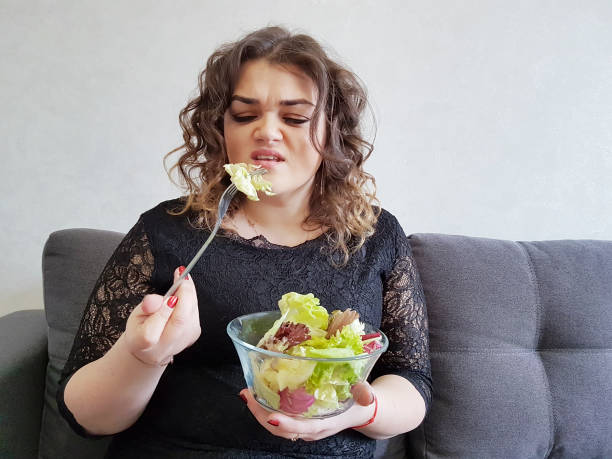 muito linda garota no sofá com uma dieta de salada - overweight women salad frustration - fotografias e filmes do acervo